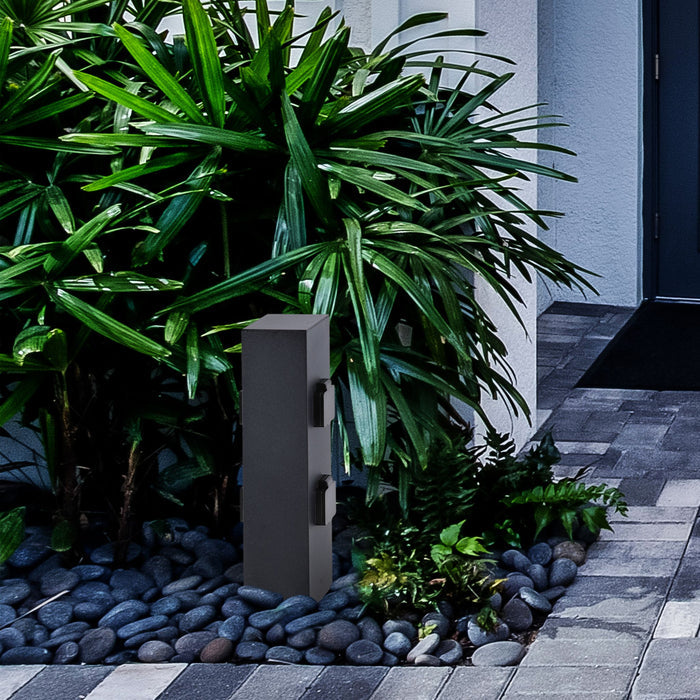 Black four socket garden power post set among pebbles and palm planting beside a paved path