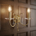 Aegean Polished Brass Double Wall Light with crystal accents, mounted on a dark wood-paneled wall.