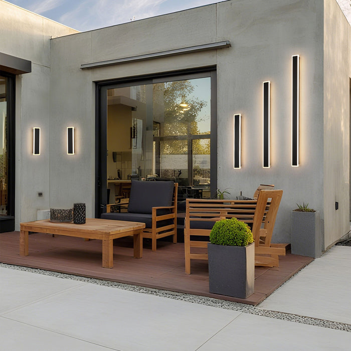 Bordo LED wall bars glowing on a concrete patio wall beside teak furniture and planters