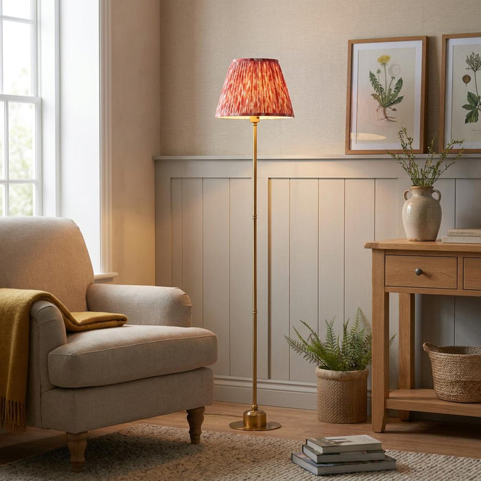 Burley brass floor lamp with a coral pink ikat shade in a cozy living room beside a beige armchair.