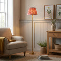 Burley brass floor lamp with a coral pink ikat shade in a cozy living room beside a beige armchair.