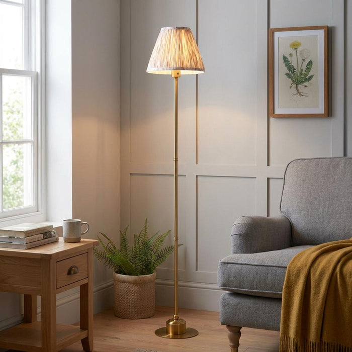 Burley brass floor lamp with a patterned ikat shade lighting up a cozy living room corner with a grey armchair.