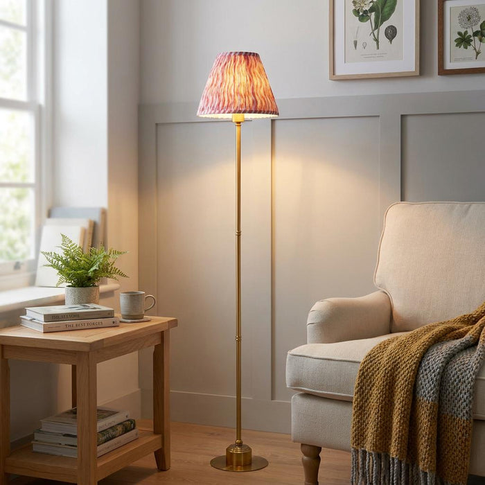 Burley brass floor lamp with a coral pink ripple shade illuminates a cozy living room next to a cream armchair.
