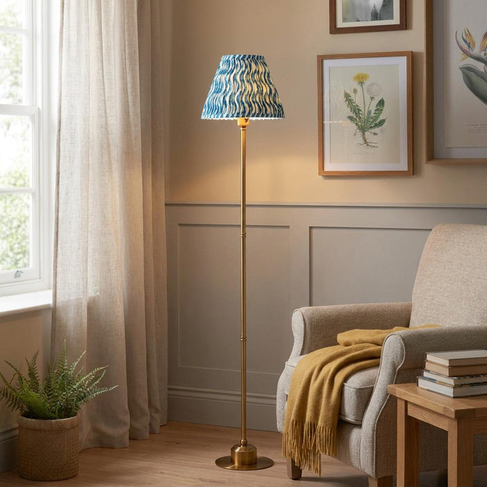 A brass floor lamp with a blue ripple shade glows next to a comfortable armchair in a warm living room.