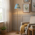 A brass floor lamp with a blue ripple shade glows next to a comfortable armchair in a warm living room.