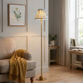 Burley brass floor lamp with a grey ripple shade standing next to a cozy armchair in a living room.