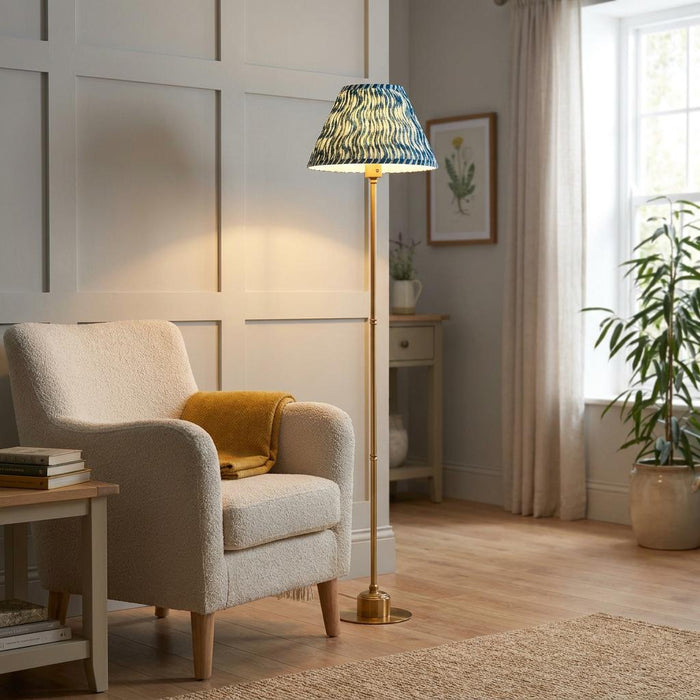 A brass floor lamp with a blue ripple shade standing next to a cream armchair in a living room.