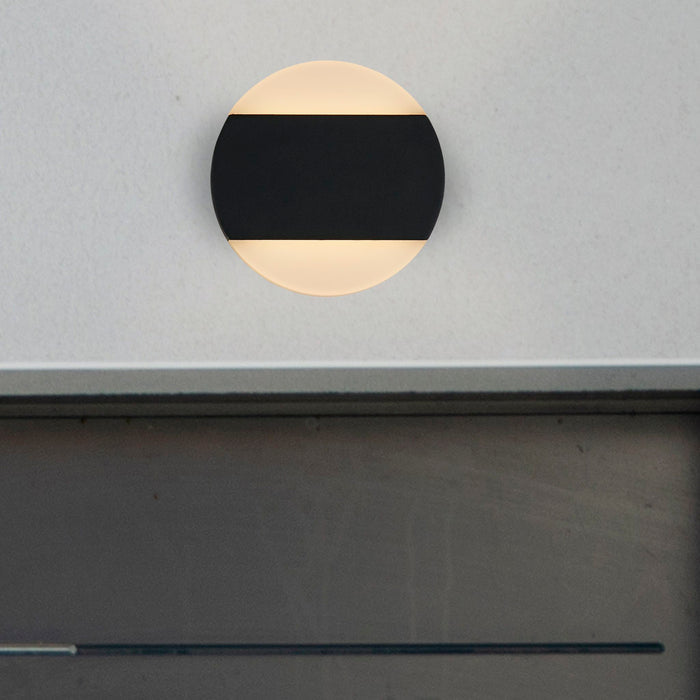 Cavern black disc wall light glowing on a pale grey wall above a dark ledge