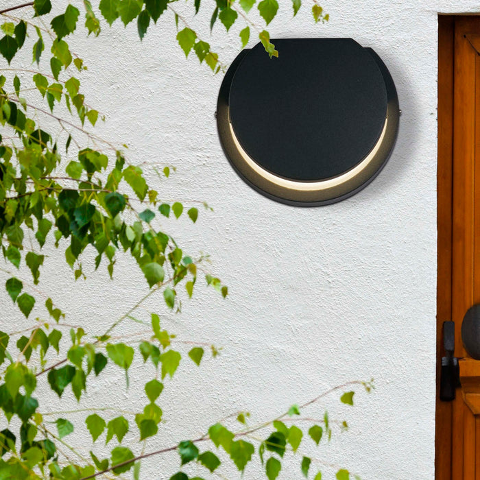 Chiswick black disc wall light on a white rendered wall beside a timber door and birch foliage