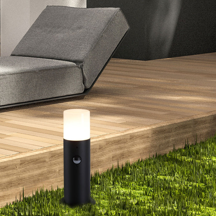 Colorado black LED bollard lit on a lawn edge beside timber decking and a grey garden sofa