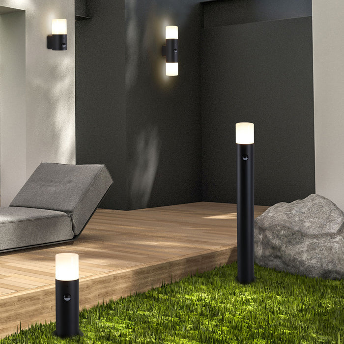 Colorado wall lights and matching bollards lit in a garden with decking a lounger and boulder