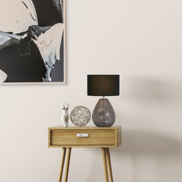 Devon glass lamp with black shade on an oak bedside table beside abstract art and ornaments