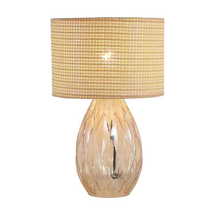 Diane champagne glass table lamp lit with a woven rattan drum shade and faceted base