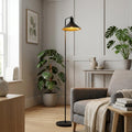 Modern black metal floor lamp with a gold interior shade standing next to a grey armchair in a cozy living room.