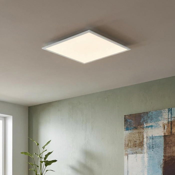 A square white LED panel light mounted flush on a neutral ceiling in a modern interior setting.