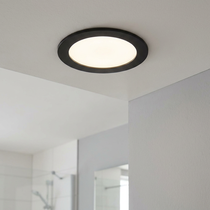 Black round LED recessed ceiling light illuminated in a modern bathroom setting.