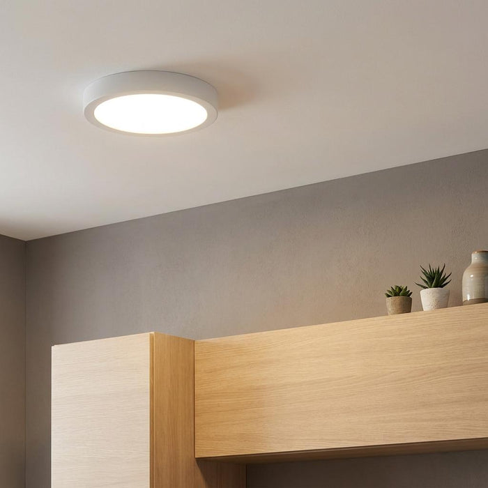 White circular LED flush mount ceiling light installed on a white ceiling above wooden cabinetry.