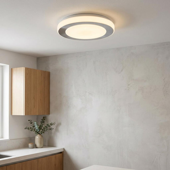 Round chrome flush ceiling light with double illuminated circles mounted on a white ceiling in a modern room.