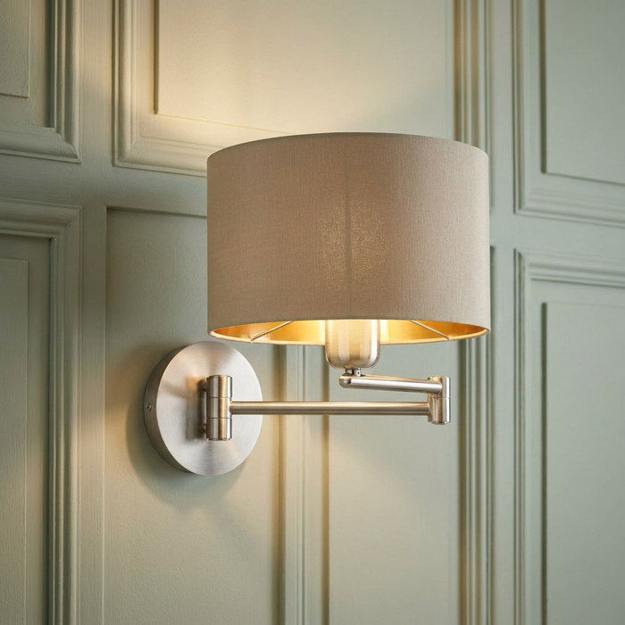Eglo Maserlo nickel swing arm wall light with a taupe shade and gold interior on a green panelled wall.