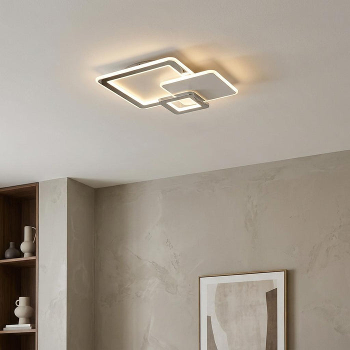 Modern chrome three-square LED flush ceiling light illuminating a minimalist room with a warm glow.