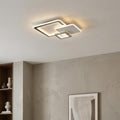 Modern chrome three-square LED flush ceiling light illuminating a minimalist room with a warm glow.