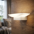 Curved white LED wall light with a warm glow mounted on a natural wood-grain wall in a living room.