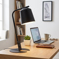 Black metal desk lamp with a conical shade illuminating a wooden workspace with a laptop and succulent.