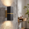 Black and gold rectangular up-and-down wall light mounted on a textured grey concrete wall in a modern room.