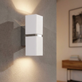 Modern white rectangular wall light with chrome accents casting light up and down on a textured grey wall.