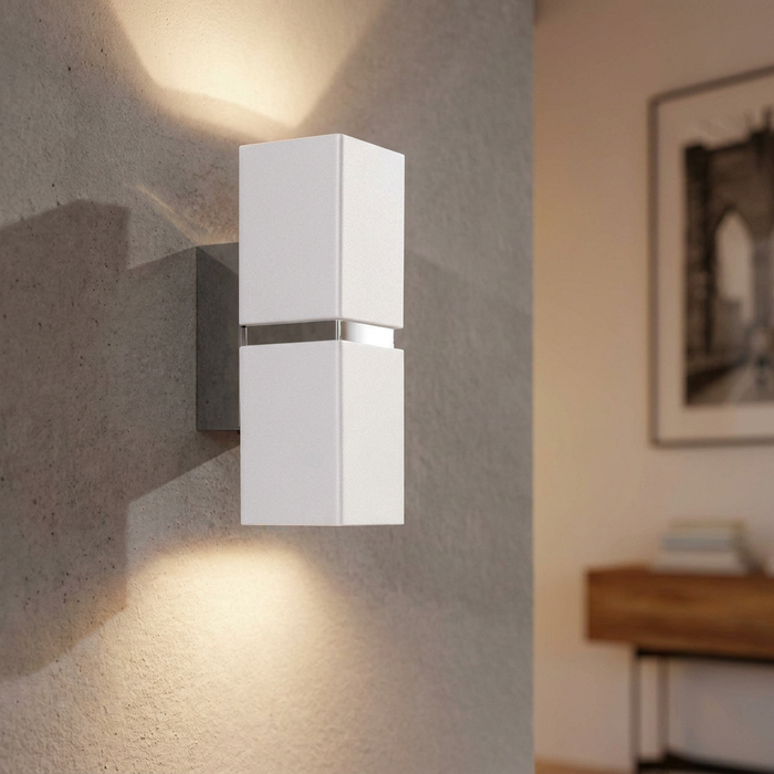 Modern white rectangular wall light with chrome accents casting light up and down on a textured grey wall.