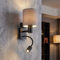 Black wall lamp with a grey fabric drum shade and flexible reading light mounted on a textured wall.