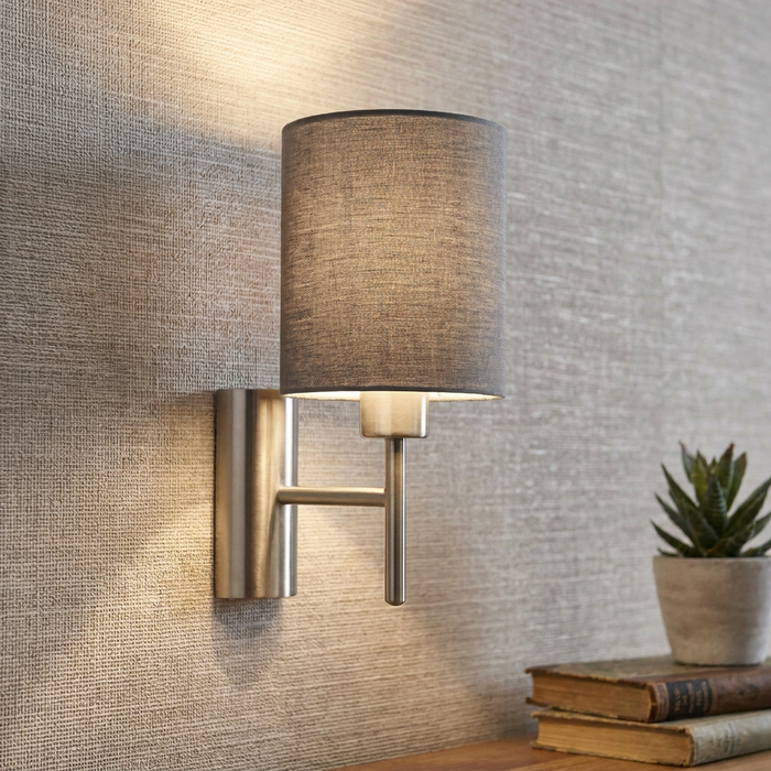 Modern brushed nickel wall light with a grey fabric drum shade mounted on a textured wallpaper background.