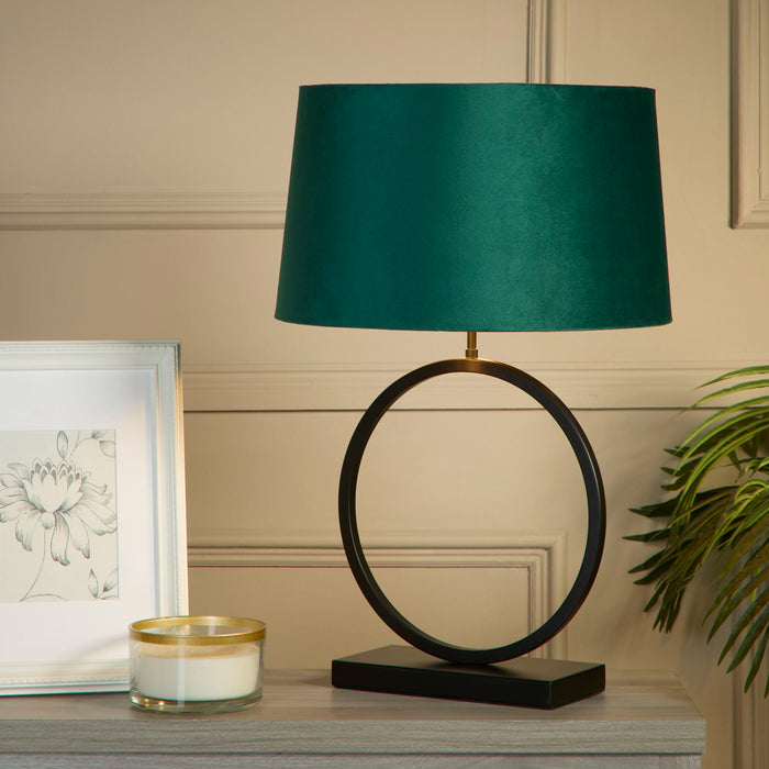 Elegant black ring lamp lit on a grey sideboard beside a framed floral print and candle