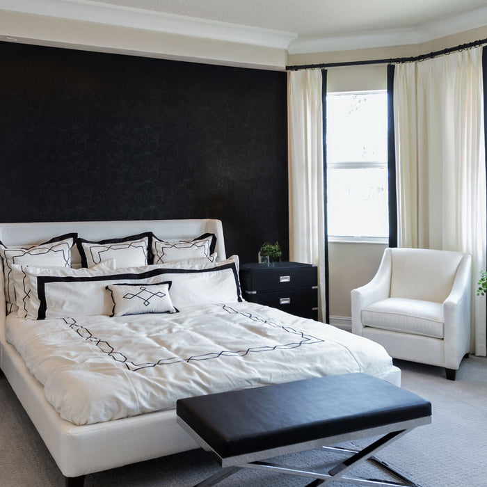 Elegant bedroom with black feature wall, white bed and cream armchair styled for Empire brass lighting