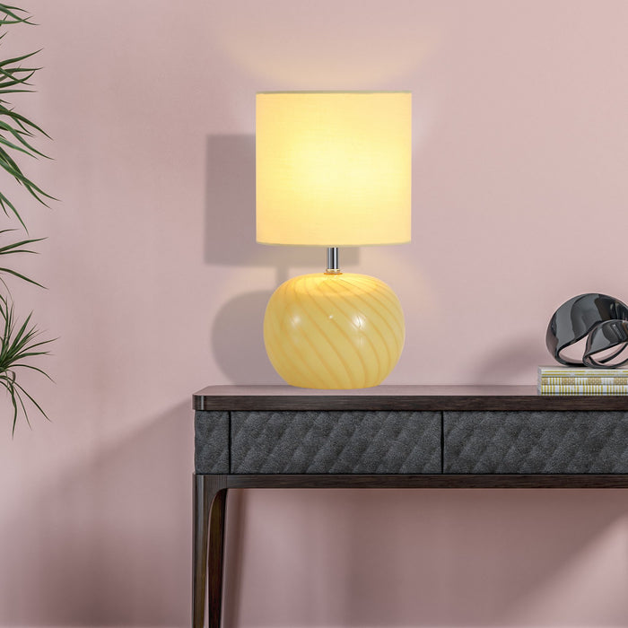 Fete yellow glass lamp on a dark console table against a soft pink wall with books