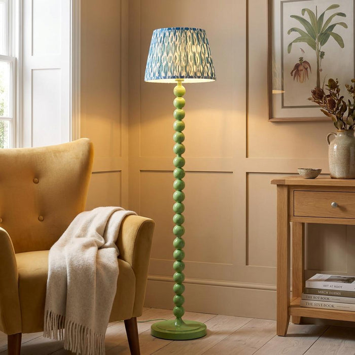 Higgledy green bobbin floor lamp with a blue ikat shade next to a yellow armchair in a paneled living room.