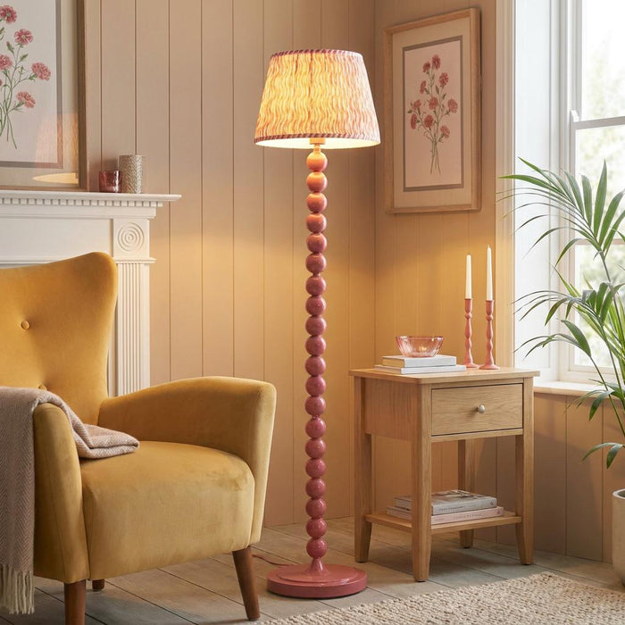 Pink floor lamp with a bobbin-style base and coral ripple shade in a cozy living room.