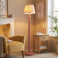Pink floor lamp with a bobbin-style base and coral ripple shade in a cozy living room.