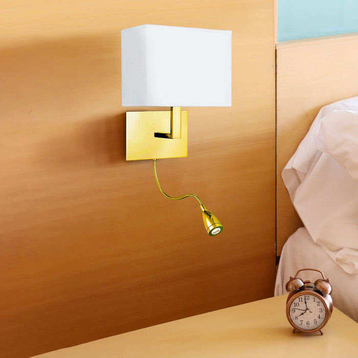 Hotel brass wall light with white shade above a bedside table and alarm clock in a bedroom