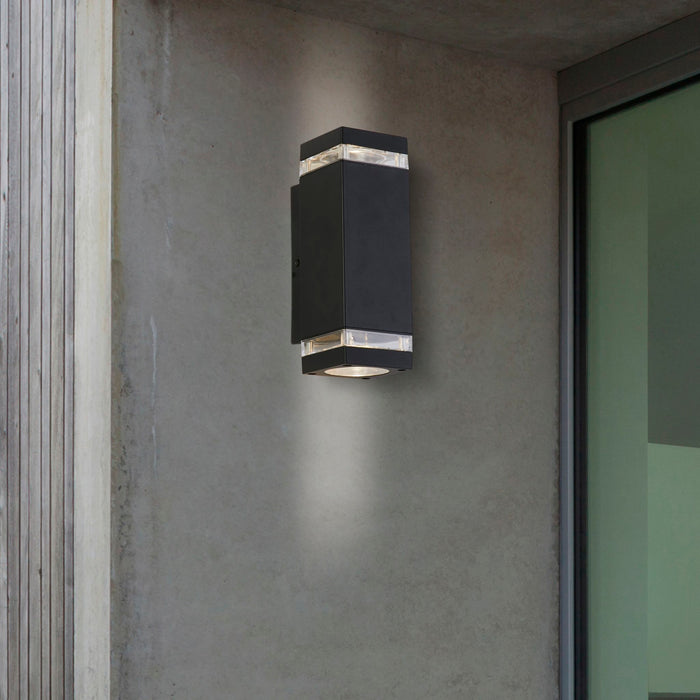 Houston black up and down wall light on a concrete house wall beside a frosted glass door at dusk
