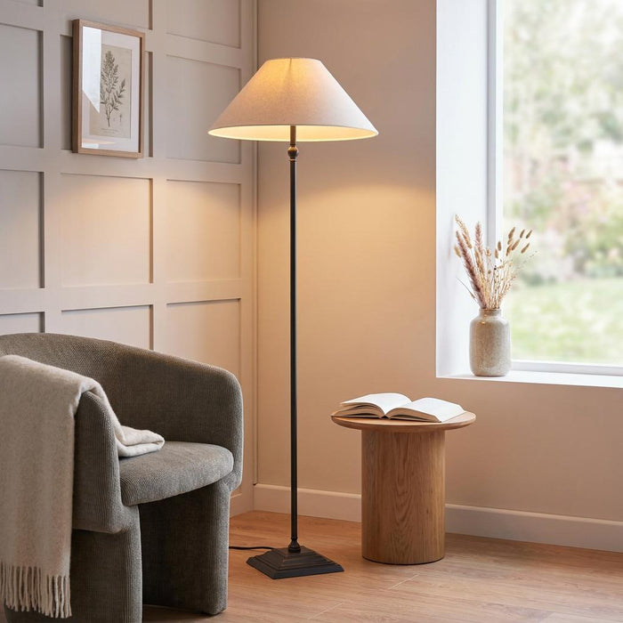 Lille floor lamp with an antique black base and cream linen shade standing in a cosy living room reading corner.