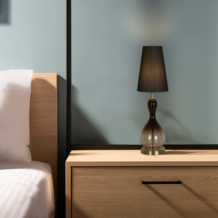 Marakesh table lamp lit on an oak bedside drawer unit beside a bed with white linen and blue wall
