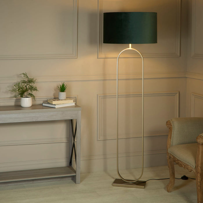 Modish bronze floor lamp with green velvet shade lit beside a grey console table and carved chair