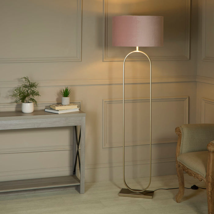 Modish bronze floor lamp with pink shade lit in a hallway beside a grey console table and armchair
