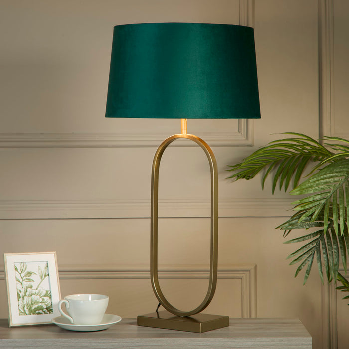 Modish emerald velvet lamp on a grey desk with teacup framed botanical art and palm fronds