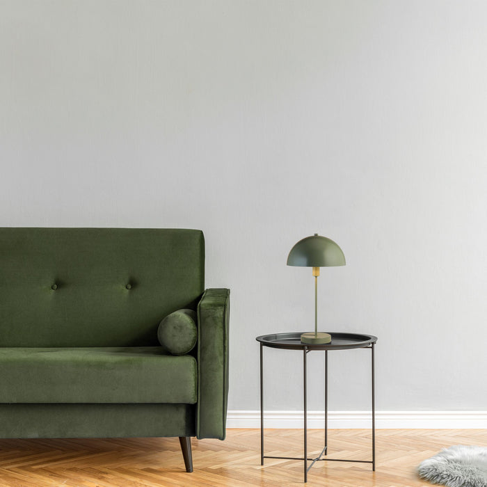 Matt green Mushroom lamp on a black tray table beside a green velvet sofa and herringbone floor