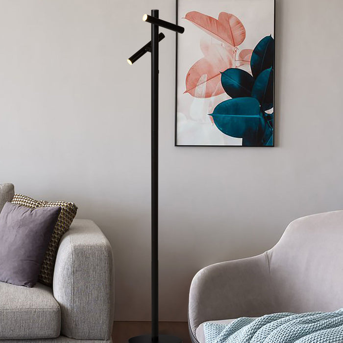 Black twin-head LED floor lamp in a living room by a grey sofa, cushions and botanical wall art