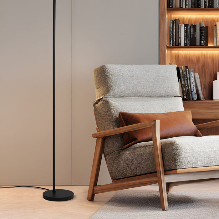 Matt black reading floor lamp beside a bouclé armchair in a study with a wooden bookcase