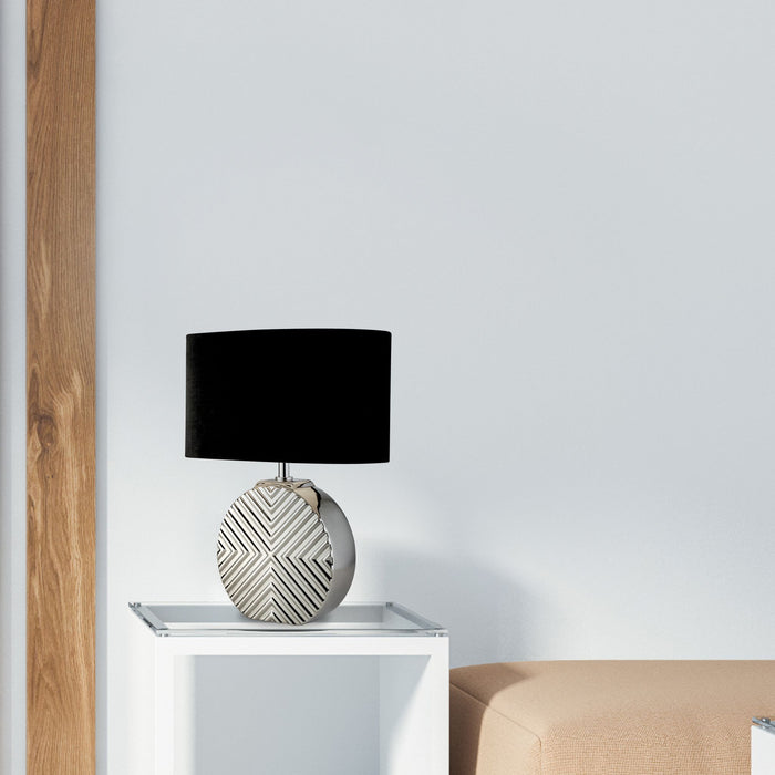 Regent chrome lamp on a white glass side table in a bright living room beside a beige ottoman