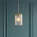 An illuminated antique brass pendant light with a cylindrical ribbed glass shade against a dark teal paneled wall.